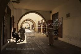 Image du Maroc Professionnelle de  Dans une rue des Habous, la succession des balèvres, moulure, arches, portiques et autres éléments décoratifs, projetent les visiteurs dans l’ardeur avec un élan de force et de fierté d’une époque révolue. Conçu par les architectes Auguste Cadet et Edmond Brion d’après l’ébauche d’un premier plan-masse dû à Albert Laprade, le quartier fait partie des endroits les plus pittoresques de Casablanca, il fut La construction n’avait commencé qu’après la première guerre mondiale. Situé près du Palais Royale, ce joyau architectural fait partie du patrimoine architectural de la ville, Samedi 8 Novembre 2008. Au centre le minaret de La mosquée Ben Youssef. (Photo / Abdeljalil Bounhar)
 